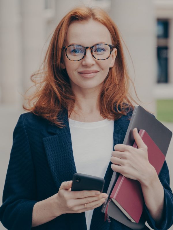 confident-beautiful-red-haired-female-business-consultant-holding-modern-smartphone-and-laptop.jpg